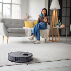 Frau sitzt auf Sofa und Saugroboter arbeitet