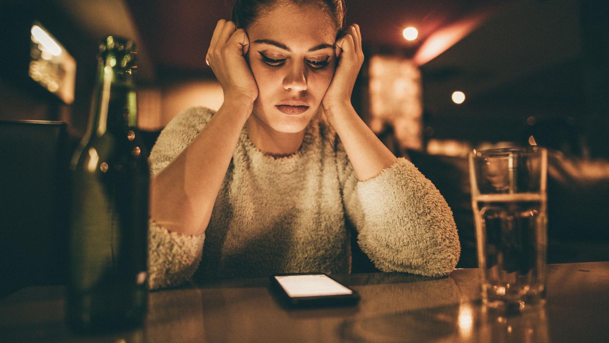Love Scam: Eine Frau sitzt alleine in einer Bar Love Scam: Eine Frau sitzt alleine in einer Bar