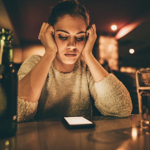 Love Scam: Eine Frau sitzt alleine in einer Bar