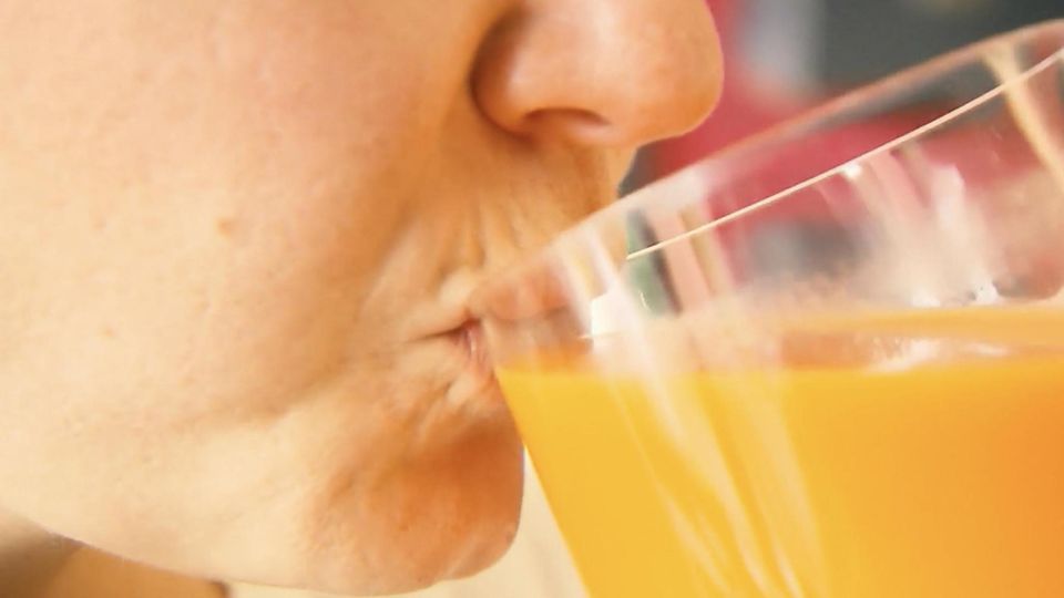 Eine Person nimmt einen schluck Orangensaft