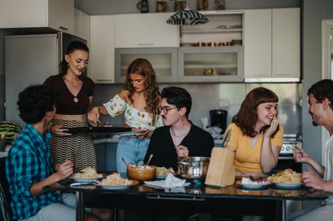 Sechs Freunde sitzen um einen Tisch und essen zusammen Spaghetti