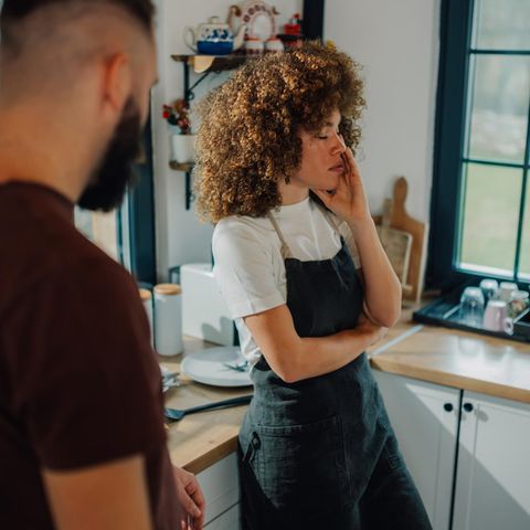 Eine Frau steht neben ihrem Mann in der Küche und hält den Kopf in der Hand