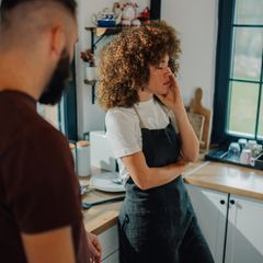 Eine Frau steht neben ihrem Mann in der Küche und hält den Kopf in der Hand