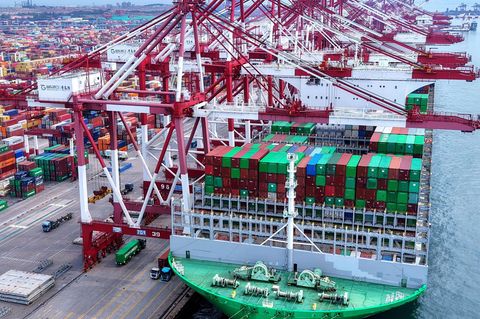 Lastwagen fahren an einem Schiff vorbei, das an einem Containerterminal in der ostchinesischen Provinz Shandong angedockt ist