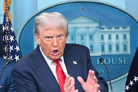 Putin rechts und Trump links stehen vor amerikanischen und russischen Flaggen bei einem Treffen und schauen ernst.