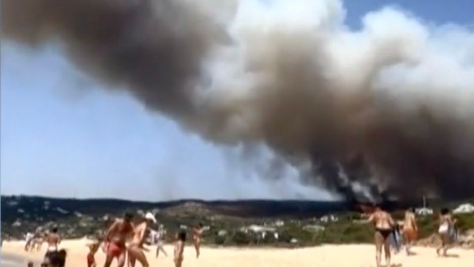 Menschen am Strand filmen Rauchschwaden.