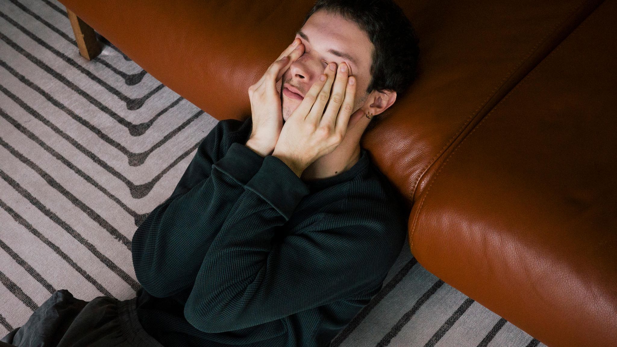 Junger Mann mit Psychose sitzt auf dem Teppich und ist an ein Ledersofa gelehnt