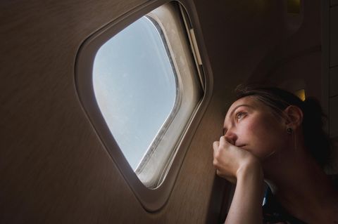 Junge Frau blickt traurig aus einem Flugzeugfenster