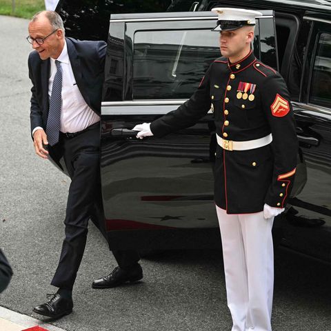 Friedrich Merz gets out of a car, the focus is on soldiers and an American flag