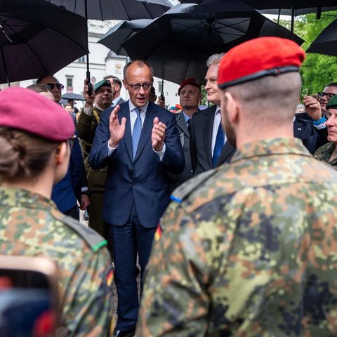 Friedrich Merz is under control umbrellas and speaks to soldiers in uniform