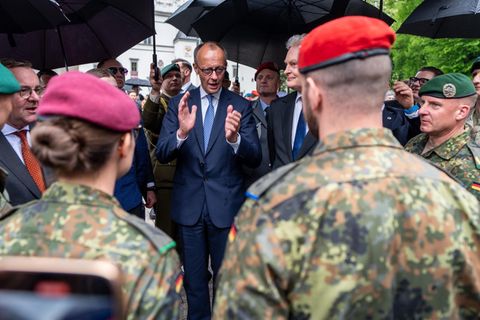 Friedrich Merz steht unter Regrnschirmen und spricht zu Soldaten in Uniform