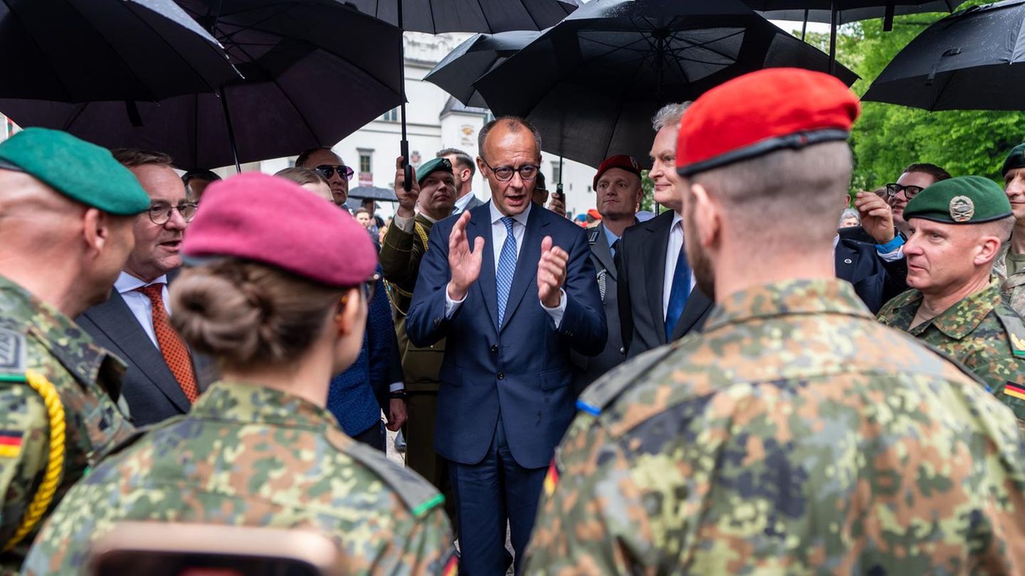 Friedrich Merz steht unter Regrnschirmen und spricht zu Soldaten in Uniform
