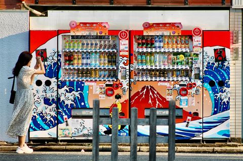Eine Frau fotografiert mit ihrem Smartphone zwei Getränkeautomaten in Tokio