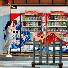 Eine Frau fotografiert mit ihrem Smartphone zwei Getränkeautomaten in Tokio
