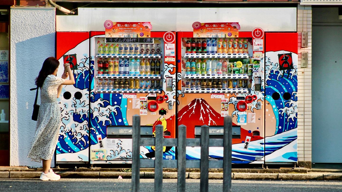 Eine Frau fotografiert mit ihrem Smartphone zwei Getränkeautomaten in Tokio
