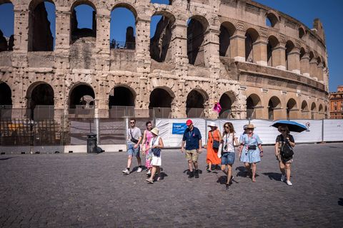 Eine Gruppe Touristen geht in praller Sonne vor dem Kolosseum in Rom entlang