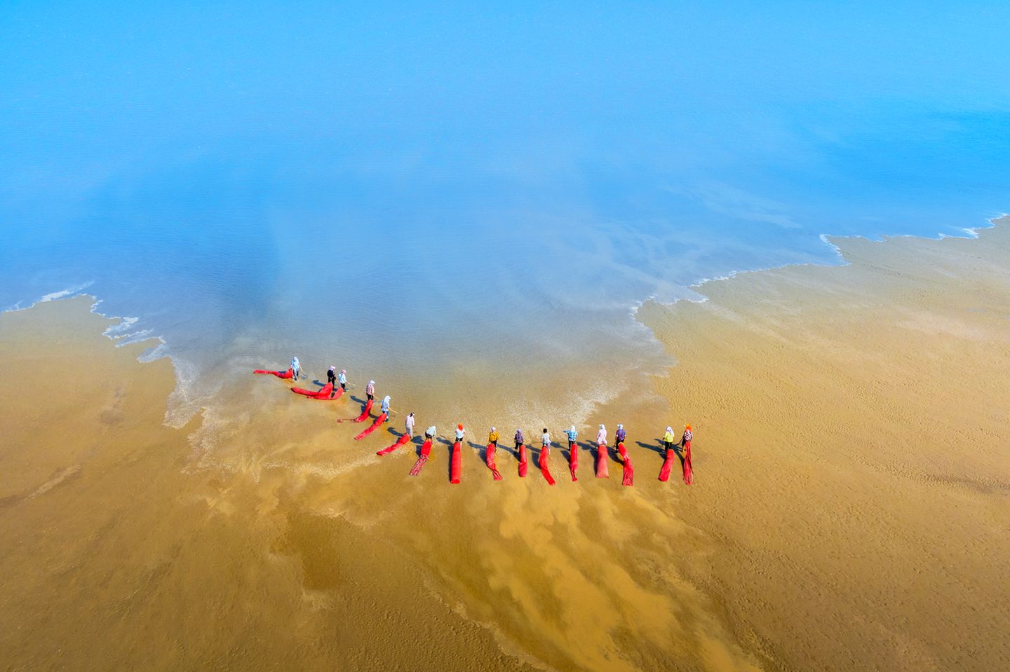 Eine Reihe von Menschen steht mit roten Netzen am Strand