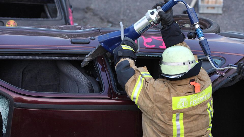 Mit einem Hydraulikspreizer öffnet ein Feuerwehrmann eine Autotür Mit einem Hydraulikspreizer öffnet ein Feuerwehrmann eine Autotür