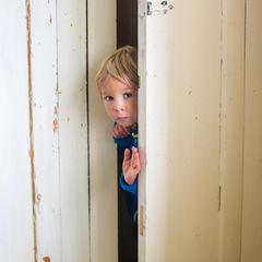 Kinder: Ein kleiner Junge guckt durch einen Türspalt