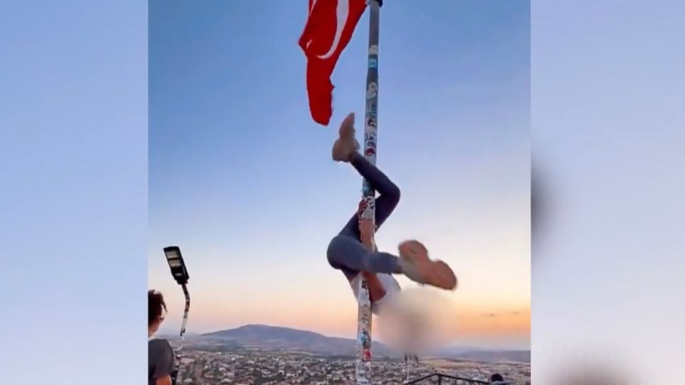 Pole-Dance an türkischer Flagge Ein Flaggenmast mit türkischer Flagge vor einem Sonnenuntergang, eine Frau schwingt sich daran rum.