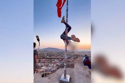 Ein Flaggenmast mit türkischer Flagge vor einem Sonnenuntergang, eine Frau schwingt sich daran rum.