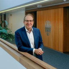 Innenminister Alexander Dobrindt lehnt im Flur seines Ministeriums am Geländer und lächelt
