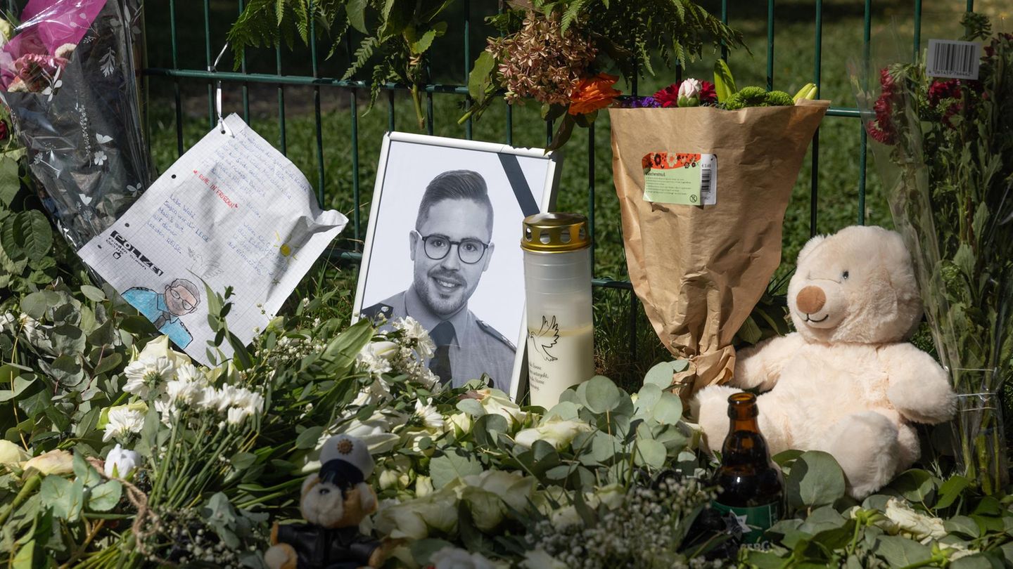 Ein Porträt des im Saarland getöteten Polizisten lehnt zwischen Blumen und Kerzen an einem Zaun