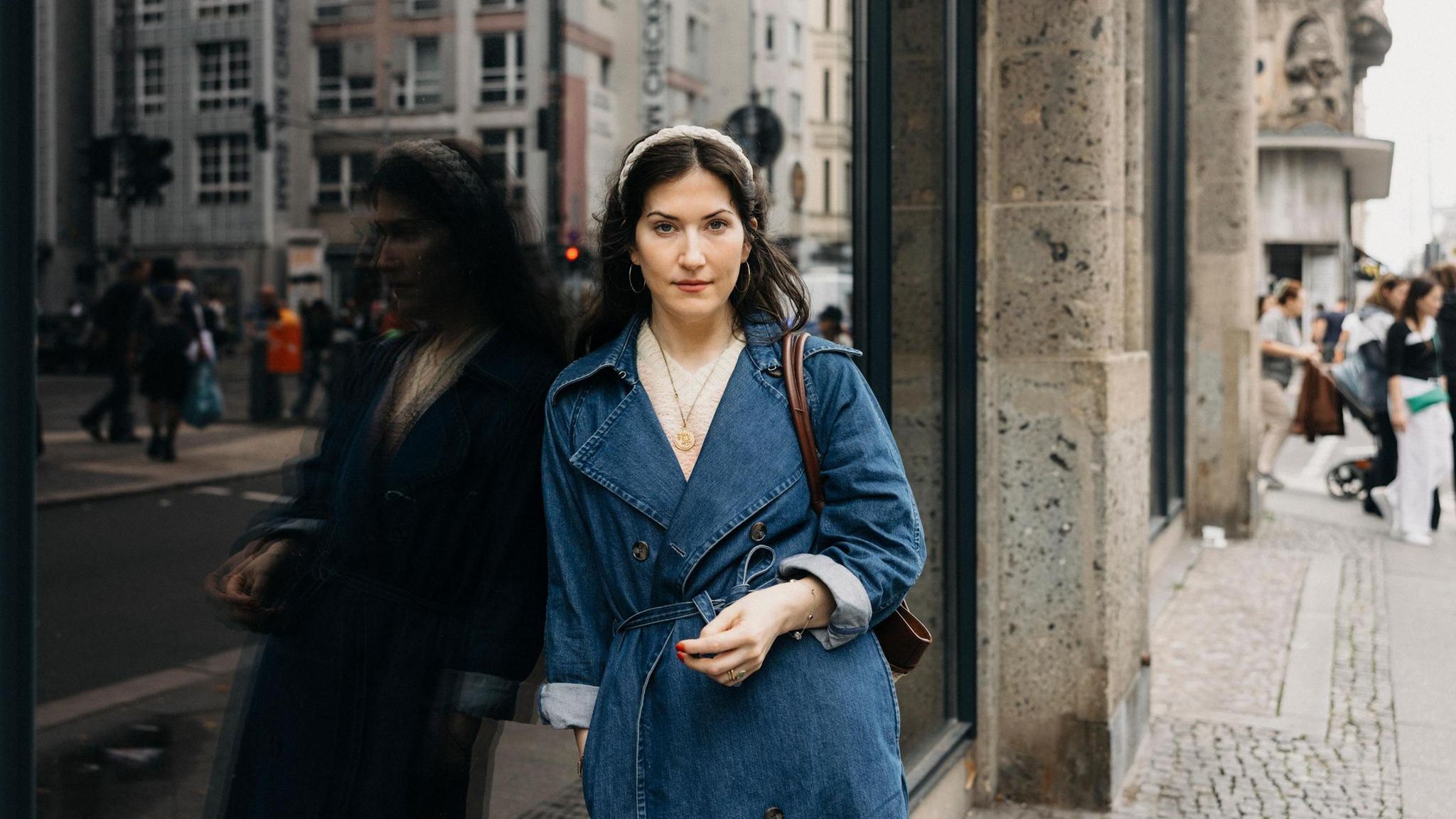 Autorin Antonia Baum im Portrait – sie trägt einen blauen Trenchcoat und lehnt an ein Fenster