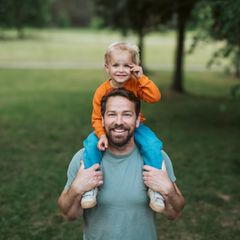 Kinderkriegen trotz Unfruchtbarkeit: ein Mann mit Kind auf den Schultern