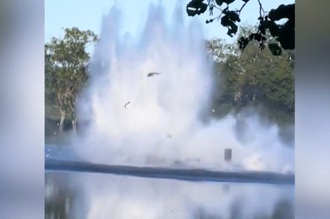 Ein Hubschrauber fliegt tief über Wasser mit einem Löscheimer, fliegt zu tief und kommt ins Wasser.