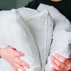 Zwei Hände halten 3 Daunenkissen fest