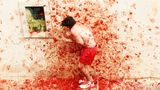 Buñol, Spanien. Ein Teilnehmer duckt sich vor der tomatenbesudelten Wand des spanischen Festspielortes Buñol, der zur Bühne des kuriosen Festes "La Tomatina" wird. Bei diesem Fest bewerfen sich die Menschen quer durch die Straßen mit Zehntausenden überreifen Tomaten, bis die gesamte Stadt in Rottöne getaucht ist. Eine fröhliche Schlacht, die seit 1945 zelebriert wird