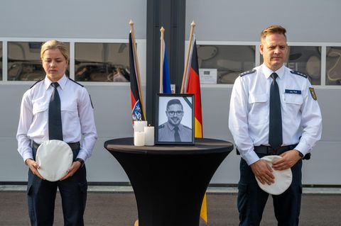 Auf einem Tisch steht ein Porträt des im Saarland erschossenen Polizisten – eine Polizistin und ein Polizist stehen daneben