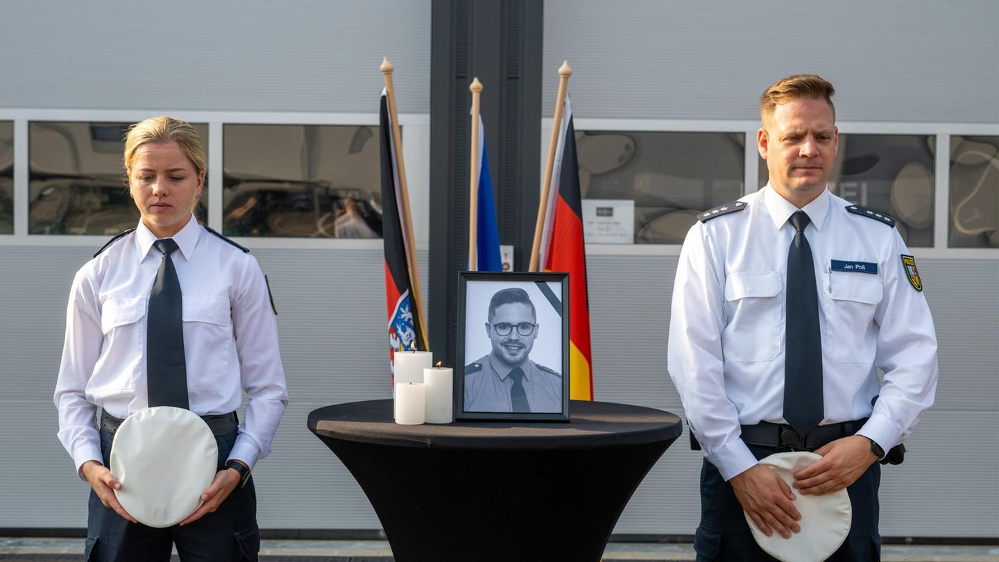 Auf einem Tisch steht ein Porträt des im Saarland erschossenen Polizisten – eine Polizistin und ein Polizist stehen daneben