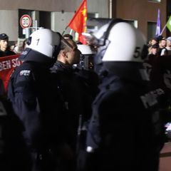 Drei Polizisten mit weißen Helmen führen einen Teilnehmer des Antikriegs-Marsches in Köln ab