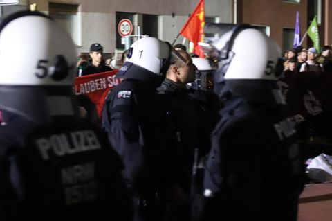 Drei Polizisten mit weißen Helmen führen einen Teilnehmer des Antikriegs-Marsches in Köln ab