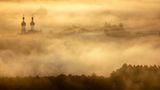 Uttenweiler, Deutschland. Die Türme der Kirche St. Simon und Judas ragen aus dem von der aufgehenden Sonne gelb gefärbten Morgennebel. Eine kleine Erinnerung daran, dass die warmen Tage gezählt sind, und man die verbleibenden genießen sollte