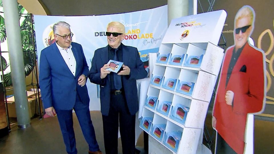 Heino hält seine eigene Tafel in der Hand neben einem Aufsteller