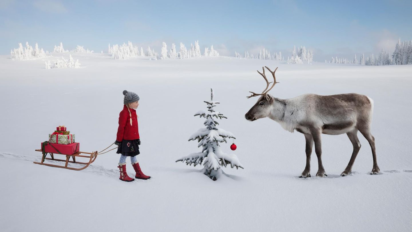 Kind mit Schlitten und Rentier im weißen Schnee