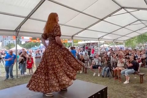 Eine Frau tanzt in langem Kleid auf der Bühne vor Menschen.