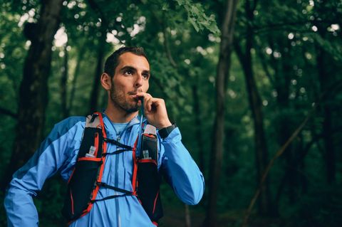 Trinkrucksack für Läufer: Trailrunner im Wald trinkt aus Trinkrucksack