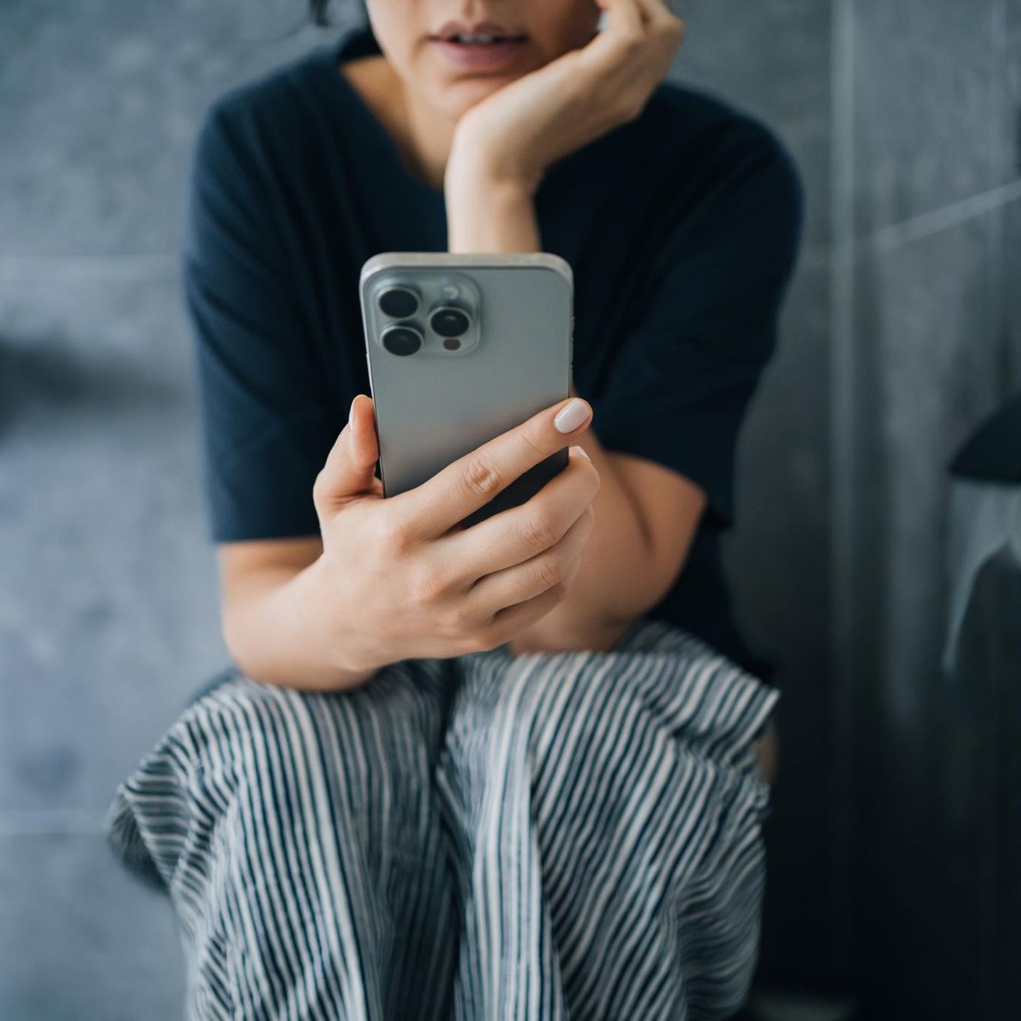 Frau mit Handy auf der Toilette – kann zu Hämorrhoiden führen