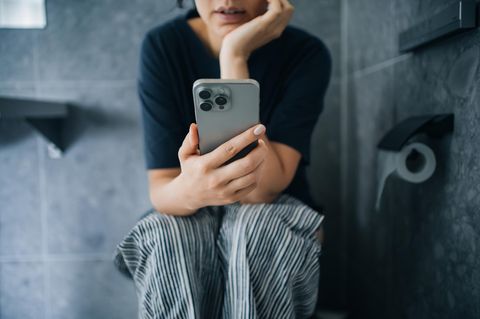 Frau mit Handy auf der Toilette – kann zu Hämorrhoiden führen