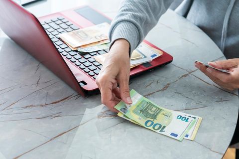 Betriebsrente Symbolbild: Hände zählen Euro-Scheine an rotem Laptop