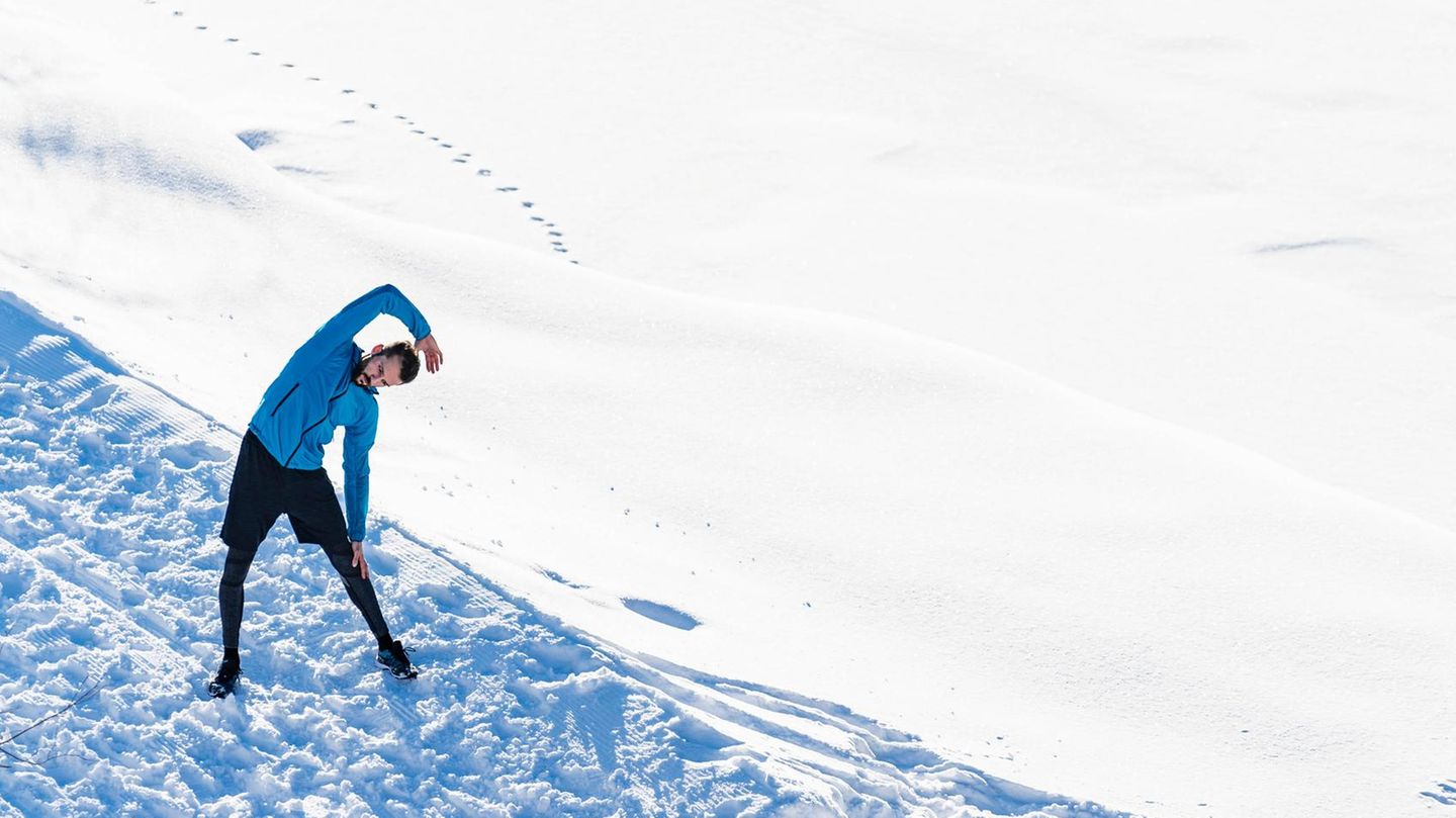 ein Mann steht im Schnee und dehnt sich