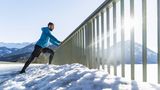 Ein Mann dehnt an einem Geländer abgestützt seine Waden