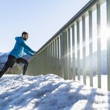 Ein Mann dehnt an einem Geländer abgestützt seine Waden