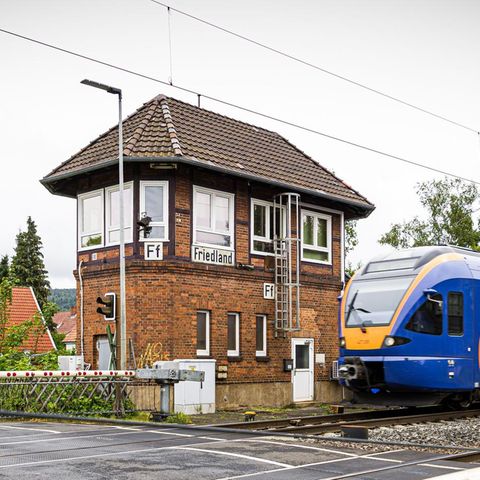Der Bahnhof von Friedland in Niedersachsen. Eine Bahnschranke, ein Zug und ein Backsteingebäude sind zu sehen