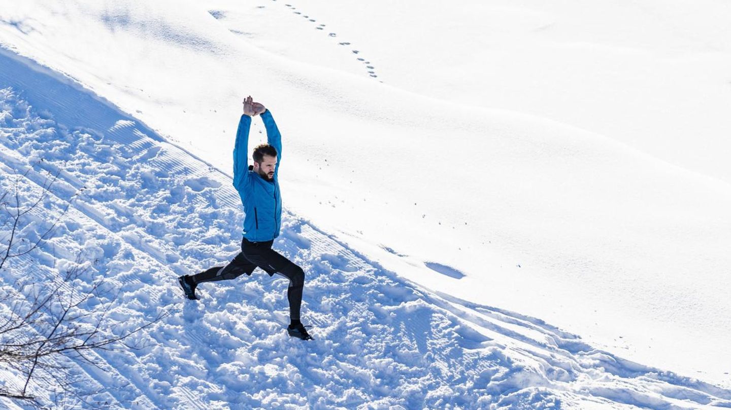 Ein Mann steht im Schnee und dehnt sich mit dem Ausfallschritt