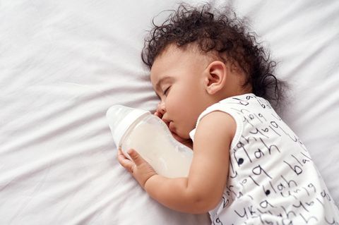 Muttermilch: Baby hält Flasche im Arm